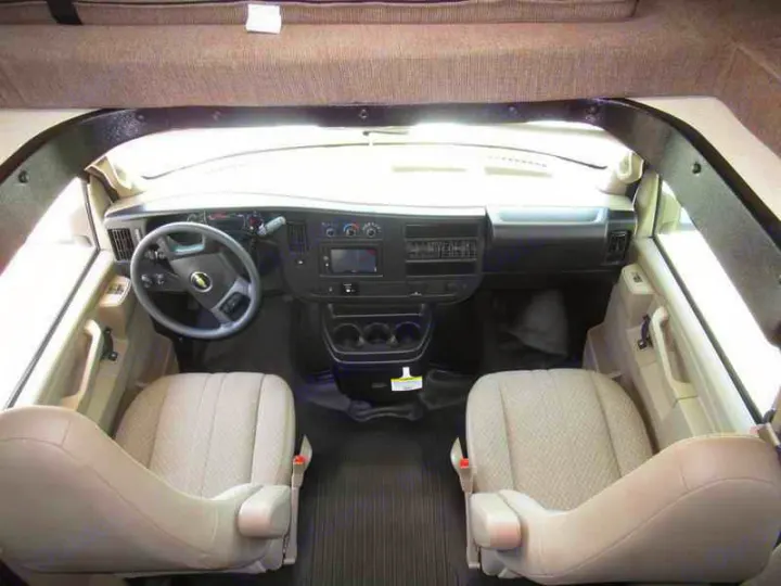 RV rental interior: driver's area with steering wheel, dash, and front seats. Overhead bunk visible.. Coachmen Freelander 2019
