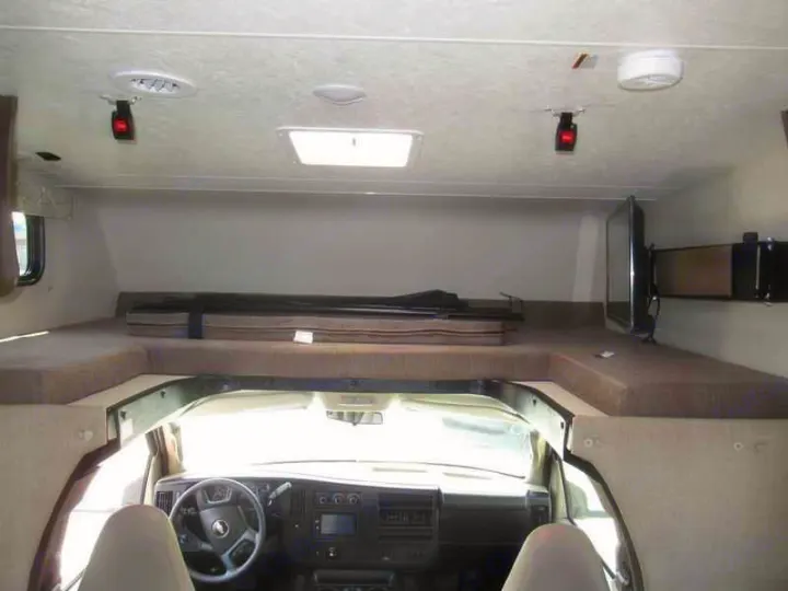 This RV rental interior features a spacious cab-over bunk bed, TV, and front cockpit view, ideal for travel.. Coachmen Freelander 2019