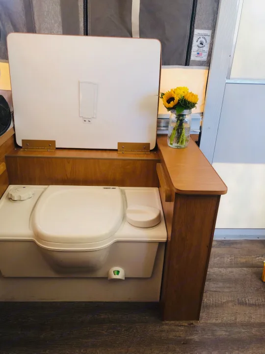 This rv rental pop-up camper features a compact toilet area. White portable toilet, wood cabinetry, and sunflowers add charm.. Coleman Grand Tour Carmel 2003