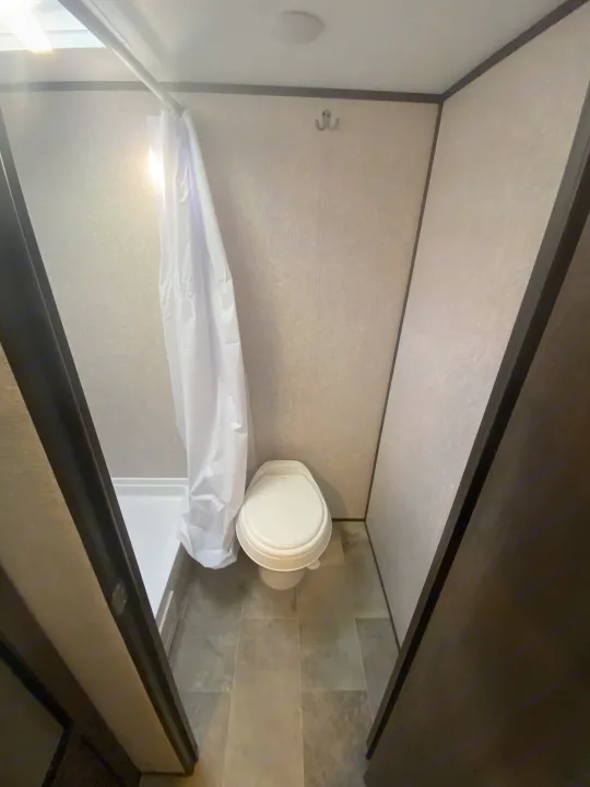 An RV rental bathroom interior, showing a white toilet, shower stall with curtain, and wall hooks in a compact layout.. Coleman Lantern 17 B 2022