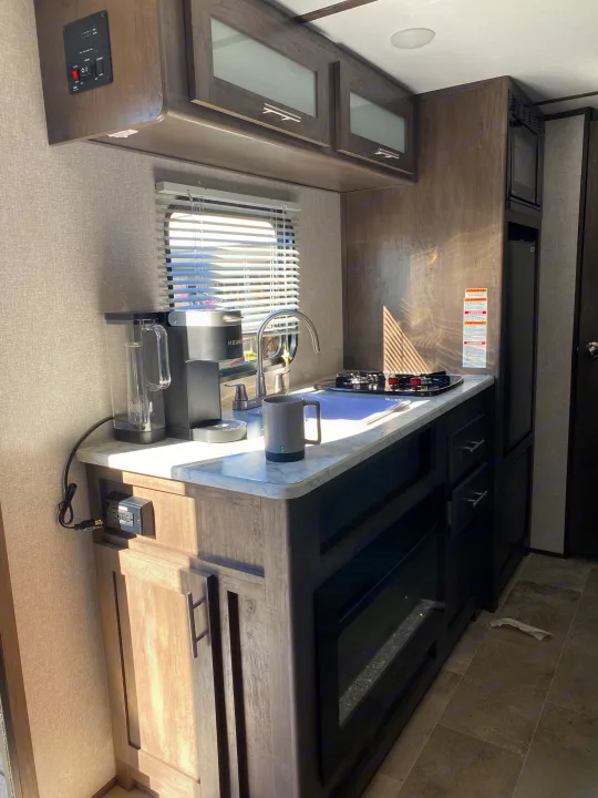 Bright RV rental kitchen showcasing compact design: counter with sink, stove, coffee maker, upper cabinets, and appliances.. Coleman Lantern 17 B 2022