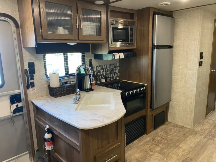 Modern RV rental kitchen with full appliances including sink, stove, microwave, and refrigerator.. Gulf Stream Trailmaster 2020