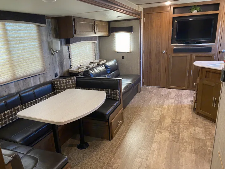 RV rental living area: Dinette with U-shaped leatherette seating, table, TV, and warm wood tones.. Gulf Stream Trailmaster 2020