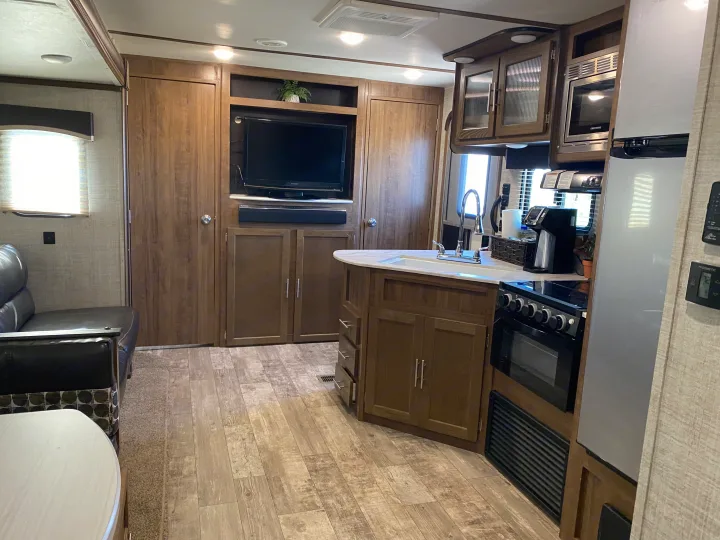 This modern RV rental interior features a compact kitchen with a sink, stove, microwave, and fridge, plus a living area with a TV and couch.. Gulf Stream Trailmaster 2020