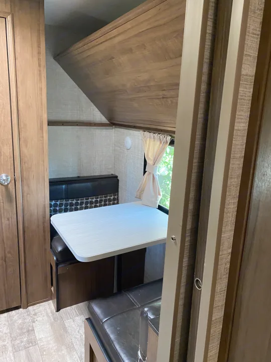 Cozy RV rental interior featuring a dinette with bench seating, a bright window, and an overhead bunk bed.. Gulf Stream Trailmaster 2020