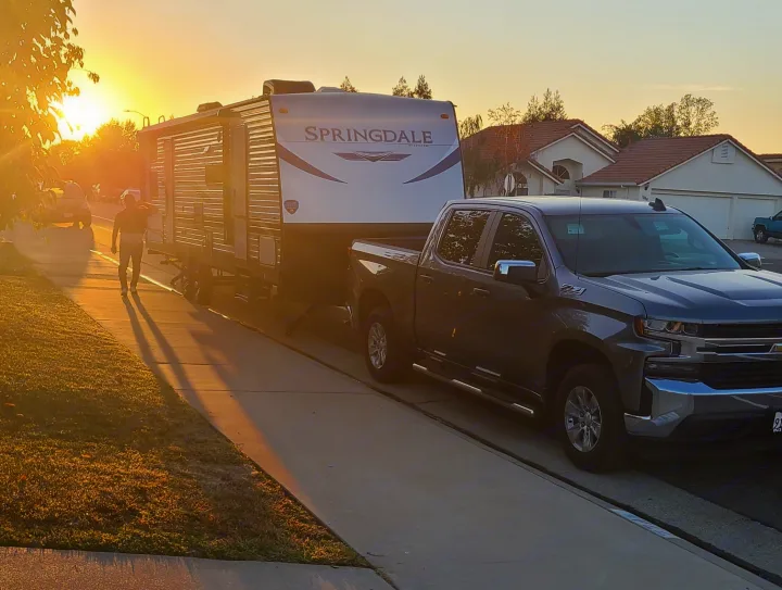 A man walks past a large gray pickup truck towing a Springdale travel trailer at sunset. Perfect RV rental setup!. Keystone Springdale 2022