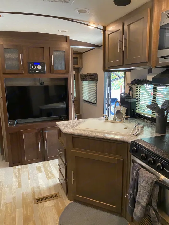 Modern rv rental interior: wood-paneled kitchen with sink, stove, and living space with TV and stereo.. Forest River Surveyor bunkhouse 2018