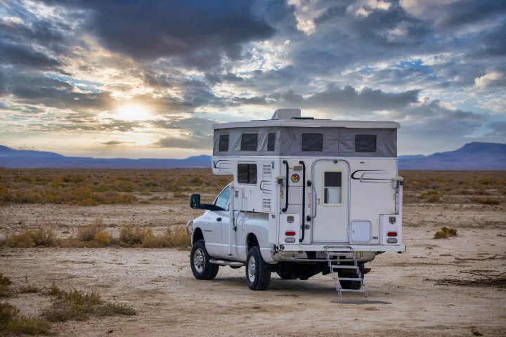 Adventure awaits! This white truck camper RV rental is perfectly parked off-grid in a stunning desert landscape at sunset.. Hallmark Everest 2011