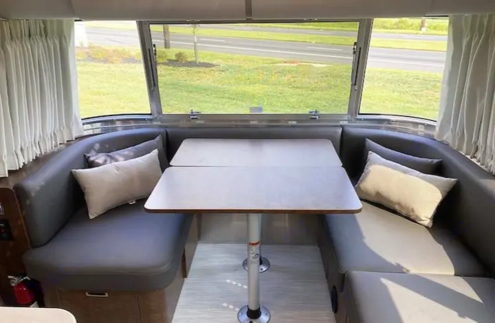 RV rental's spacious dinette: gray seating, modular table, and large windows with outdoor views.. Airstream Globetrotter 2022