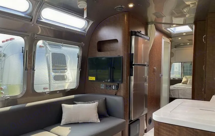 Interior of a modern Airstream RV rental, featuring a lounge with TV, refrigerator, and a glimpse into the bedroom.. Airstream Globetrotter 2022