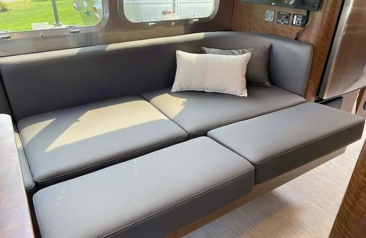 Grey upholstered modular sofa with extended seating and throw pillows inside a modern RV rental interior.. Airstream Globetrotter 2022