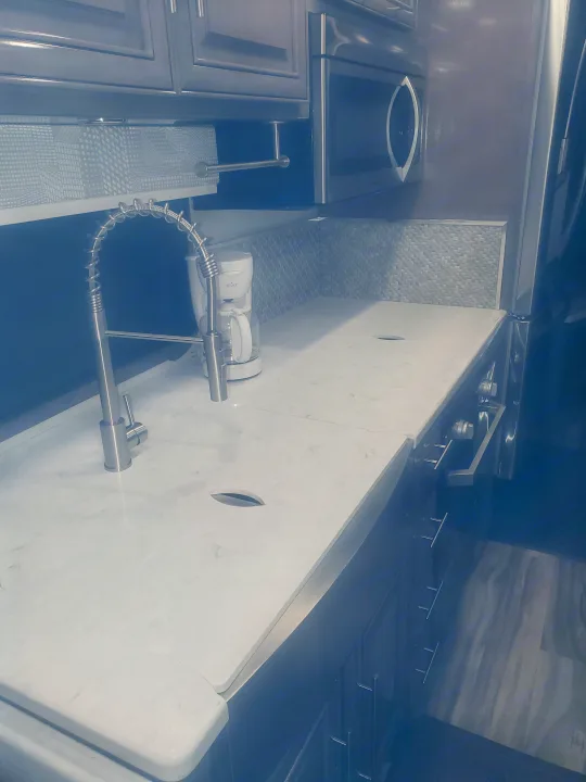 Detailed view of an RV rental kitchen showing a stylish faucet, marble-look counter, built-in microwave, and coffee maker.. Forest River Georgetown GT7 2021
