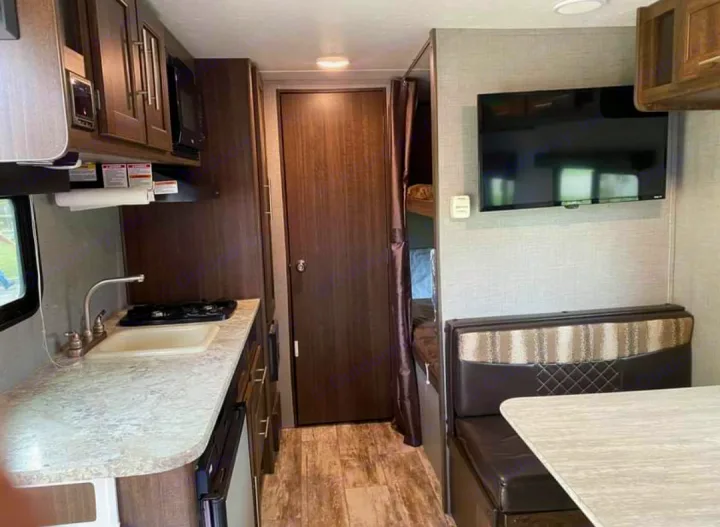 Explore this RV rental interior: a galley kitchen, bathroom door, bunk beds, and dinette with TV. Perfect for road trips!. Crossroads Zinger 2018