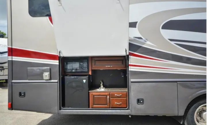 An RV rental's side compartment is open, revealing an outdoor kitchen with a microwave, mini-fridge, and sink.. Fleetwood Other 2017
