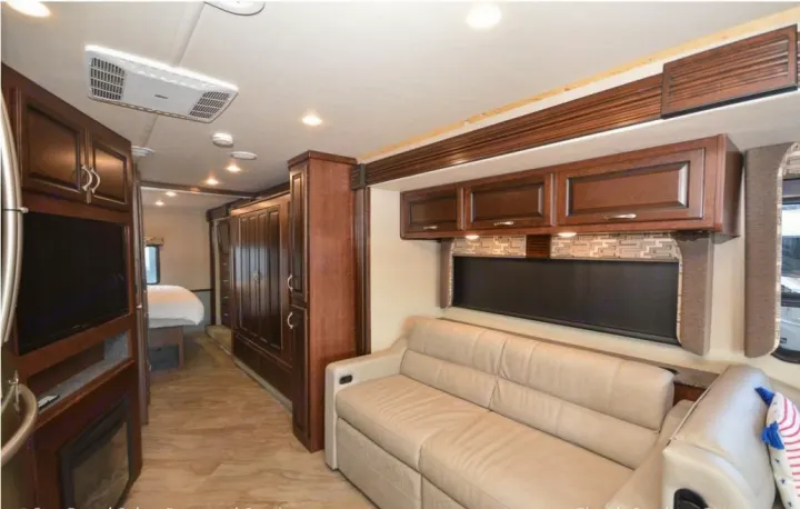 This RV rental interior features a cozy living space with a beige sofa, TV, and fireplace, leading to a private bedroom.. Fleetwood Other 2017