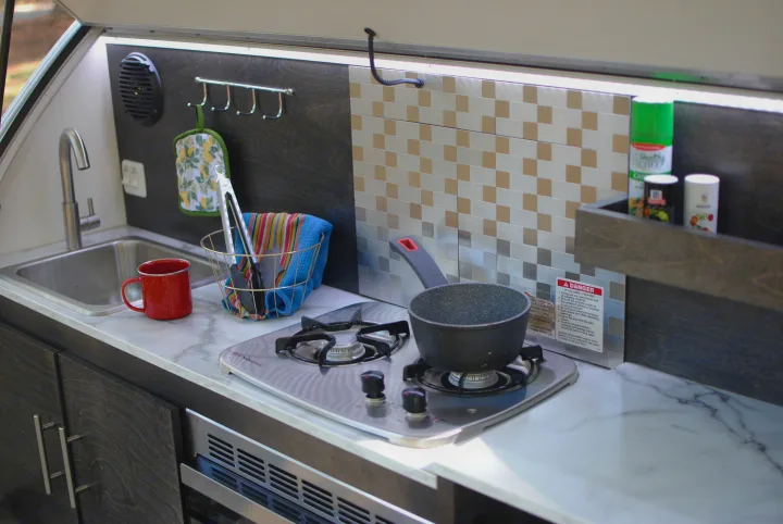 An RV rental kitchenette features a sink, two-burner stove with a pot, and counter space for compact travel cooking.. nuCamp T@G 2021