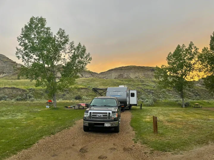 Travel trailer and truck at a peaceful RV rental campsite amidst scenic badlands and green trees.. Coachmen Catalina SBX 221TBS 2019