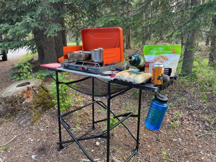 RV rental trip: Campsite cooking with a portable stove, pots, corn, and groceries amidst trees.. Coachmen Catalina SBX 221TBS 2019