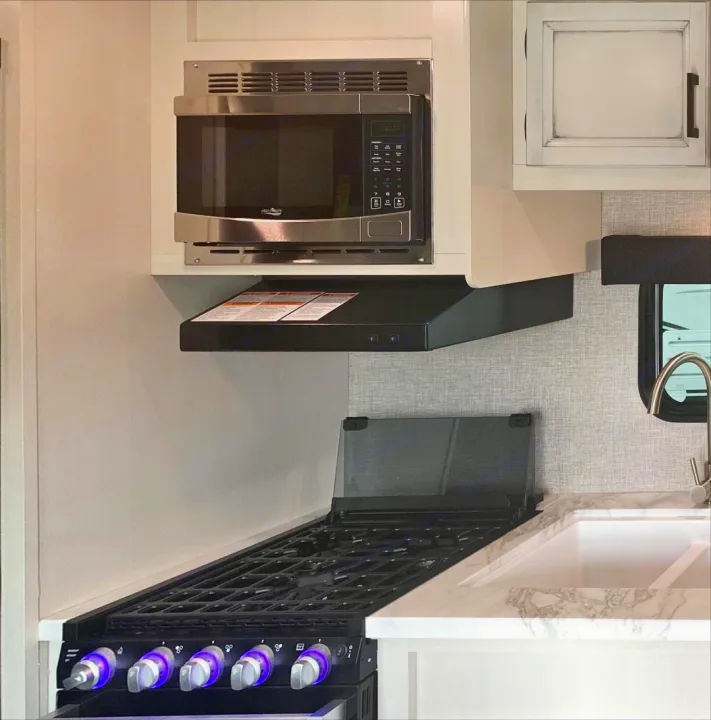 Modern RV rental kitchen featuring a microwave, range hood, gas stove with glowing knobs, and sink for compact living.. Jayco Jay Flight 2022