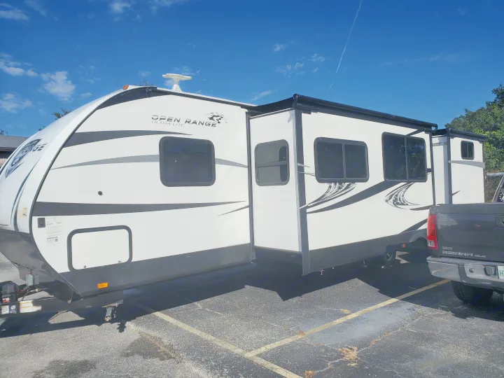 White Open Range travel trailer with slide-out, perfect for your next RV rental adventure. Parked under blue skies.. Highland Ridge RV Open Range Ultra Lite 2019