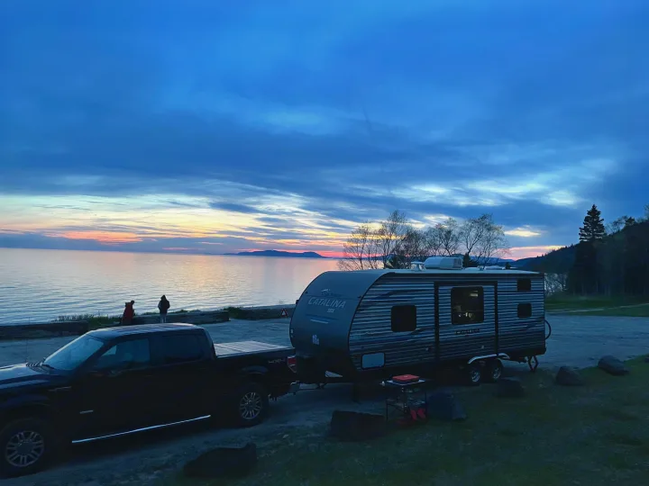 A serene lake sunset with an RV rental, pickup truck, and two people by the water, perfect for a peaceful outdoor trip.. Coachmen Catalina SBX 221TBS 2019
