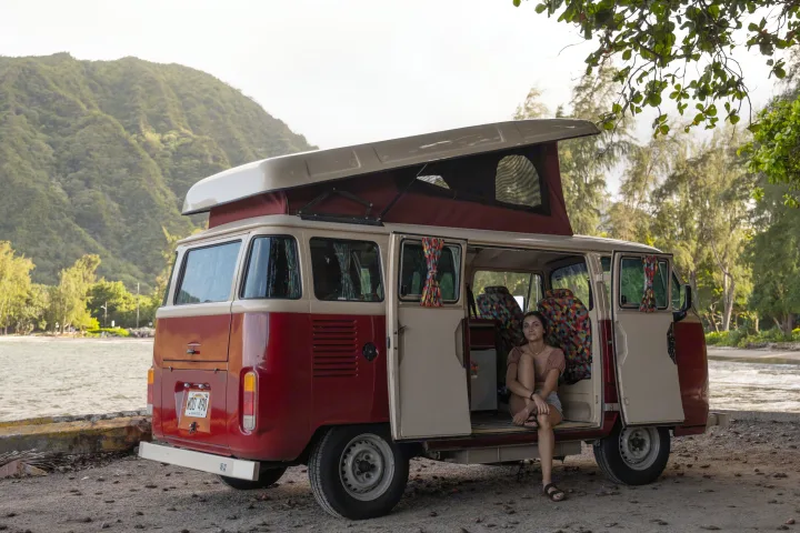 Young woman in a pop-top vintage Volkswagen camper van parked by a Hawaiian bay, ideal for your next rv rental adventure.. Volkswagen Other 1993