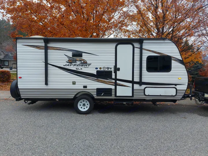A white Jayco Jay-Flight SLX RV, a great rv rental option, parked on asphalt with vibrant autumn trees in the background.. Jayco Jay Flight SLX 2019