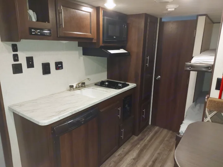 View of an RV rental's kitchen area with a sink, stove, microwave, and refrigerator. Bunk beds and a dining table are also visible.. Jayco Jay Flight SLX 2019