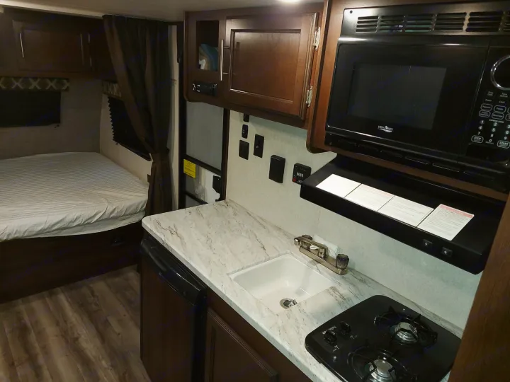 RV rental interior featuring a functional kitchen with microwave, stovetop, sink, and a comfortable bed area.. Jayco Jay Flight SLX 2019