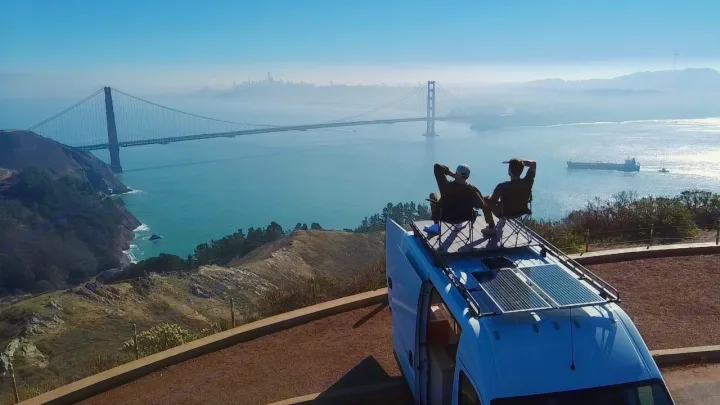 Enjoying a stunning Golden Gate Bridge view from an RV rental, two people relax on the van's roof, overlooking San Francisco Bay.. ram ProMaster 2021