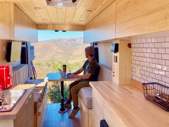 Man working on laptop in a modern rv rental camper van, enjoying scenic mountain views from his mobile workspace.. ram ProMaster 2021