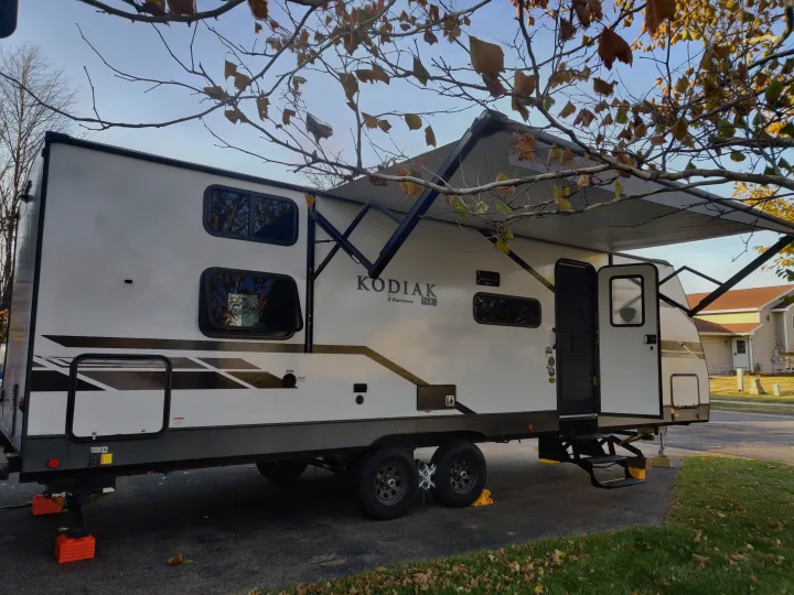Kodiak travel trailer RV rental with awning extended, parked on a driveway with autumn foliage. Ready for adventure.. Dutchmen Kodiak 2021