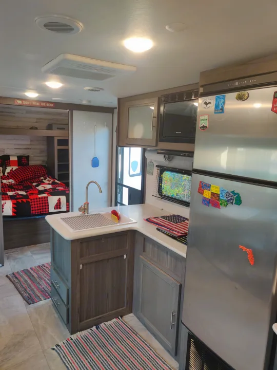Explore this bright rv rental! Features a fully equipped kitchen, stainless steel fridge, microwave, and a cozy plaid bedding.. Dutchmen Kodiak 2021