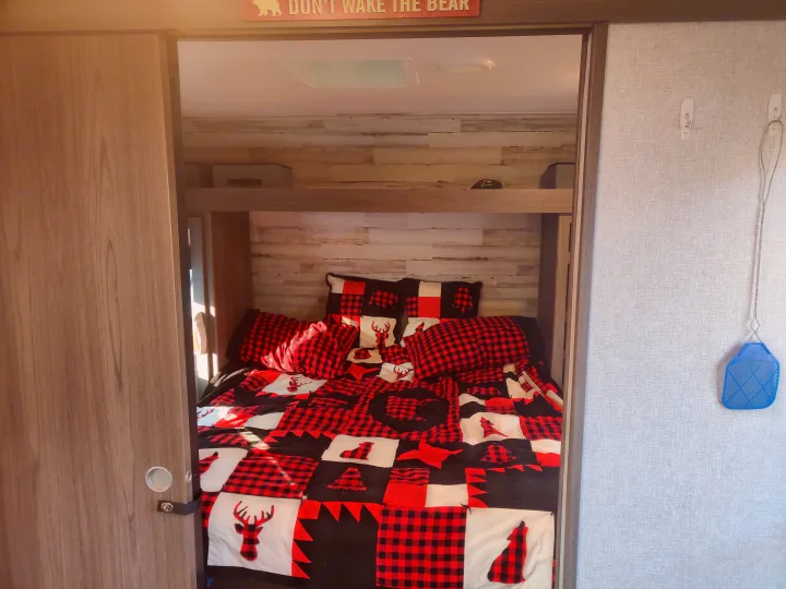 RV rental bedroom: cozy with red and black plaid bedding featuring wildlife, a bear sign, and rustic wood-look walls.. Dutchmen Kodiak 2021