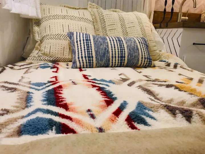 This inviting RV rental bed features textured cream and blue patterned pillows atop a cozy, colorful geometric blanket.. Scamp 13' 1979