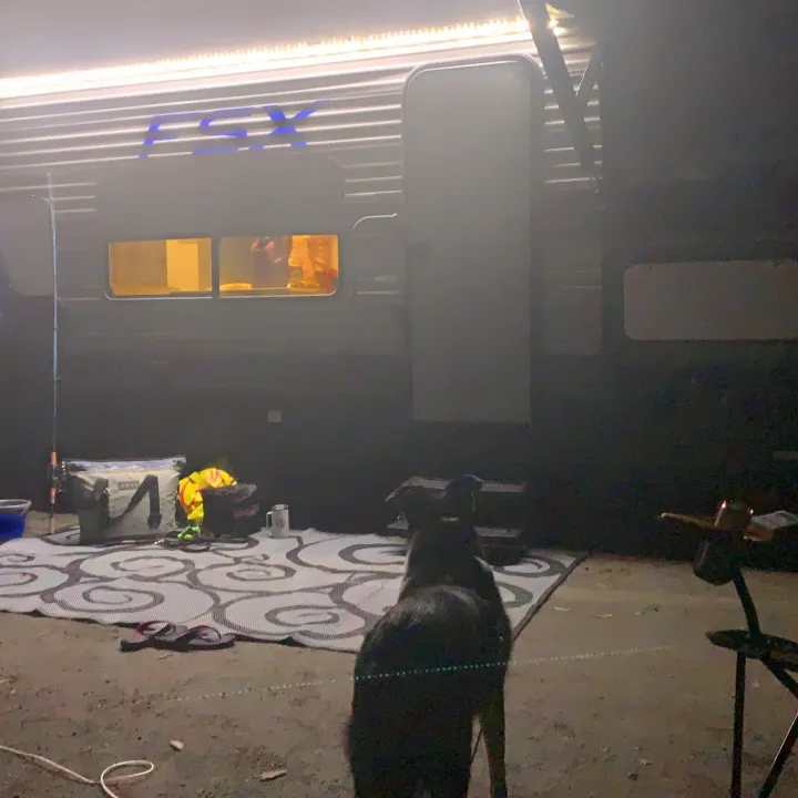 Nighttime RV rental by Fox, with a dog, camping gear on a mat, and people visible in the illuminated interior.. Forest River Salem FSX 2021