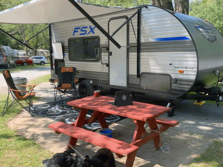 A cozy **rv rental** campsite scene with a Salem FSX travel trailer, picnic table, and dogs relaxing.. Forest River Salem FSX 2021