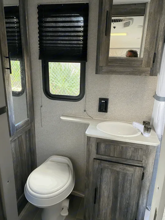 Compact rv rental bathroom with toilet, sink, window, and mirror reflecting the RV interior.. Forest River Salem FSX 2021