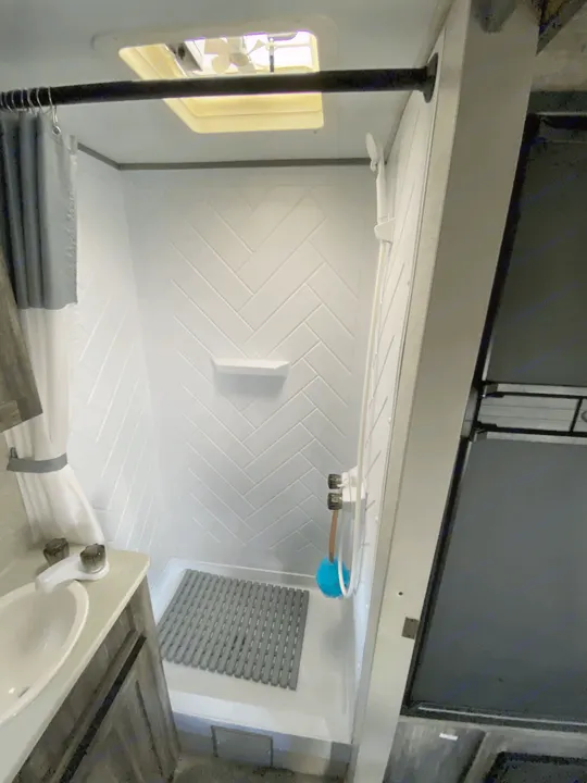 Clean RV rental bathroom showcasing a compact shower with herringbone walls, vanity, and ceiling vent for a comfortable stay.. Forest River Salem FSX 2021