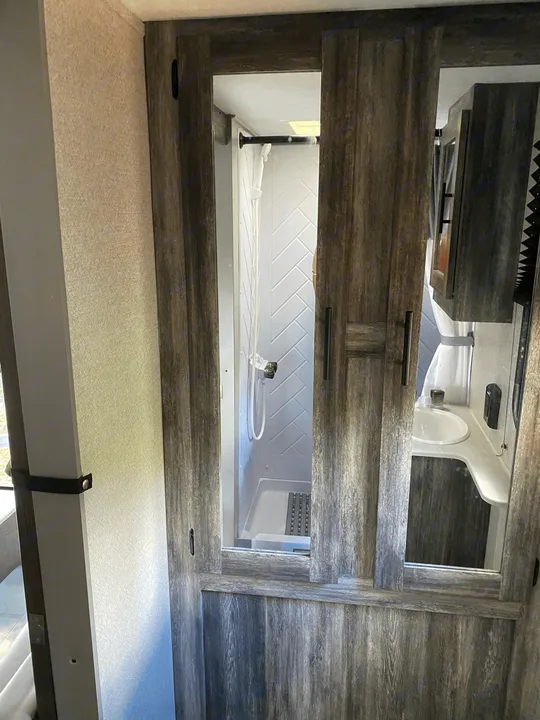Compact RV rental bathroom features a stylish shower with herringbone tiles and a functional vanity with sink.. Forest River Salem FSX 2021