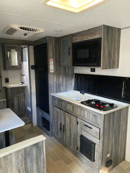Modern RV rental interior with kitchen (sink, stove, microwave), dining table, and bathroom access. Perfect for travel adventures.. Forest River Salem FSX 2021