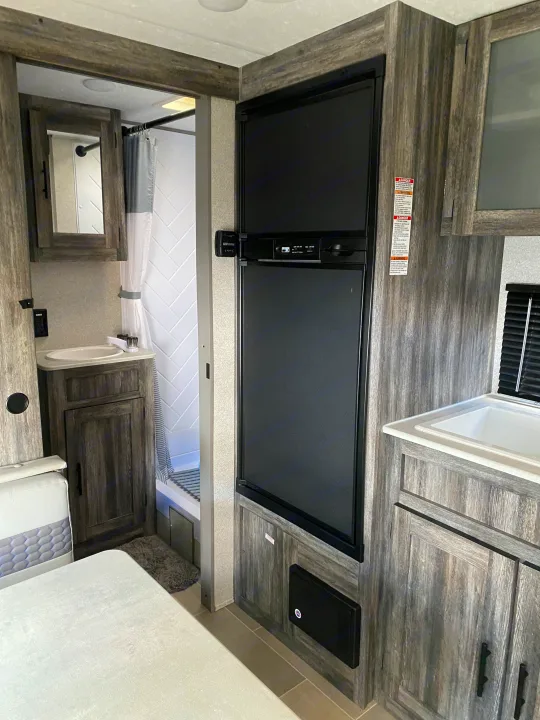 RV rental interior features bathroom, large refrigerator, and kitchen space with rustic wood cabinets.. Forest River Salem FSX 2021