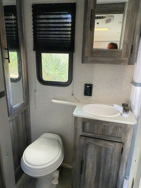 RV rental bathroom features: a compact toilet, sink with cabinet, and mirror reflecting ceiling & user.. Forest River Salem FSX 2021