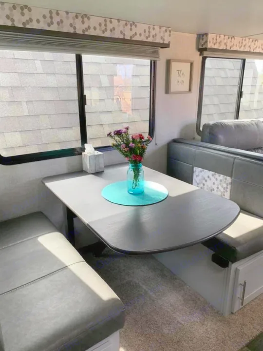 Cozy RV rental dinette with dark table, gray benches, and bright windows. Perfect for comfortable travel adventures.. Keystone Bullet 2020