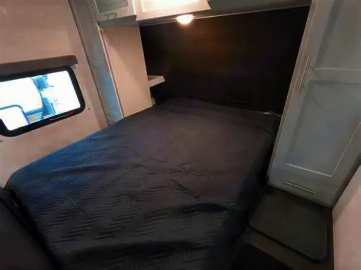Cozy RV rental bedroom featuring a dark grey bed, window, and built-in cabinets for a comfortable sleeping area.. Keystone Bullet 2020