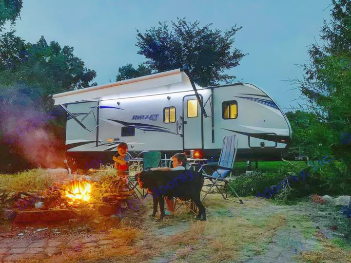 Enjoying an RV rental adventure: Kids and dog by a cozy campfire at dusk, with the bright travel trailer behind them.. Keystone Bullet 2020