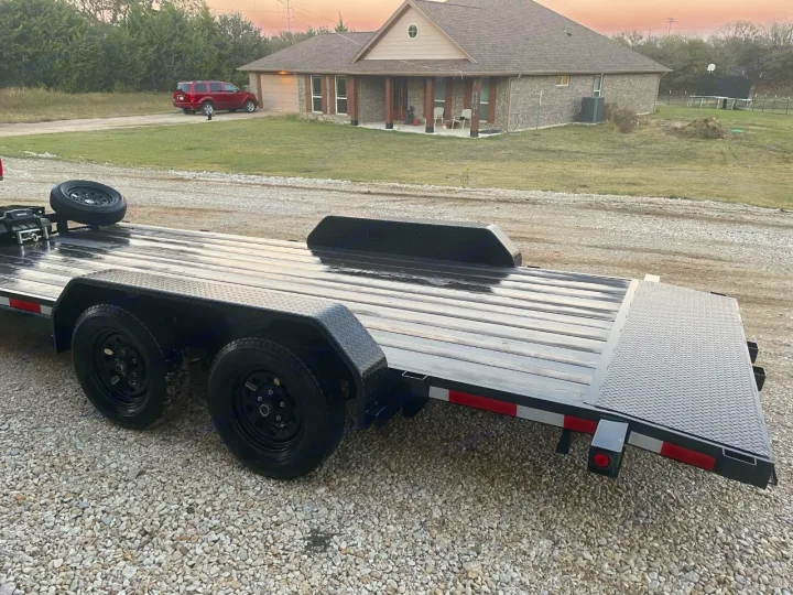 Black tandem axle flatbed trailer on gravel, ideal for equipment or vehicle transport to complement your RV rental adventures.. Other Other 2020