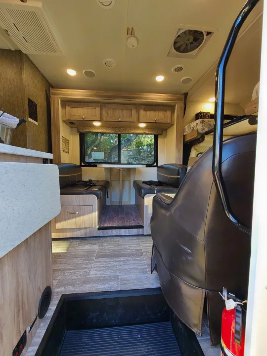 Inside an RV rental: a well-lit dinette with cushioned benches, an adjustable table, and overhead storage, looking out a window.. Forest River Sunseeker 2019