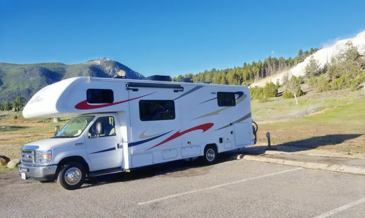 An RV rental, a white Class C motorhome, parked at Yellowstone's Mammoth Hot Springs with mountains and steam visible.. Forest River Sunseeker 2019