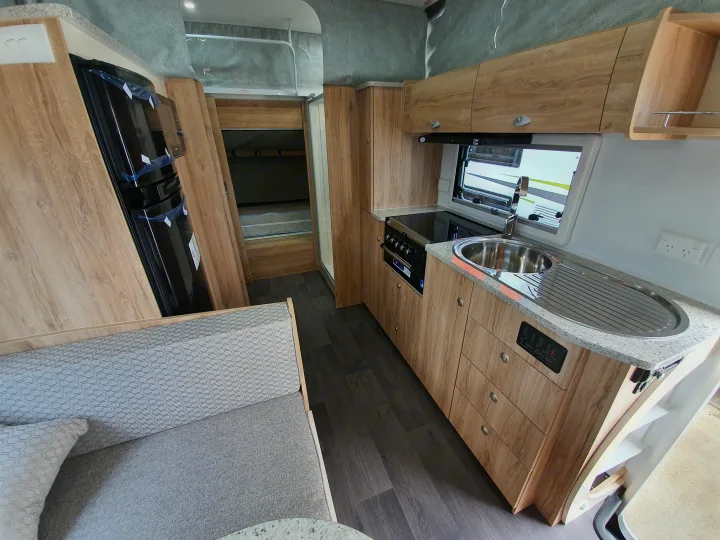 Inside an RV rental: a compact kitchen with sink, stove, and fridge, plus a living area & bunk beds.. Golf Maxxi 501-1 2021